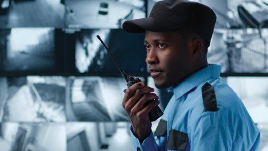 Security officer with a radio in front of CCTV screens