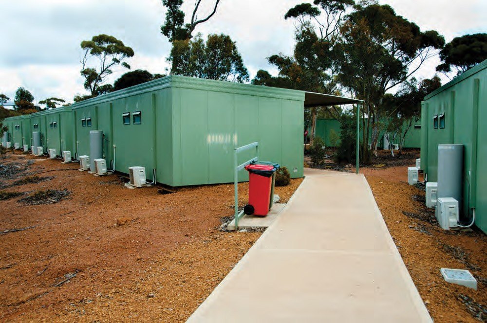 Green modular camp units along a paved walkway