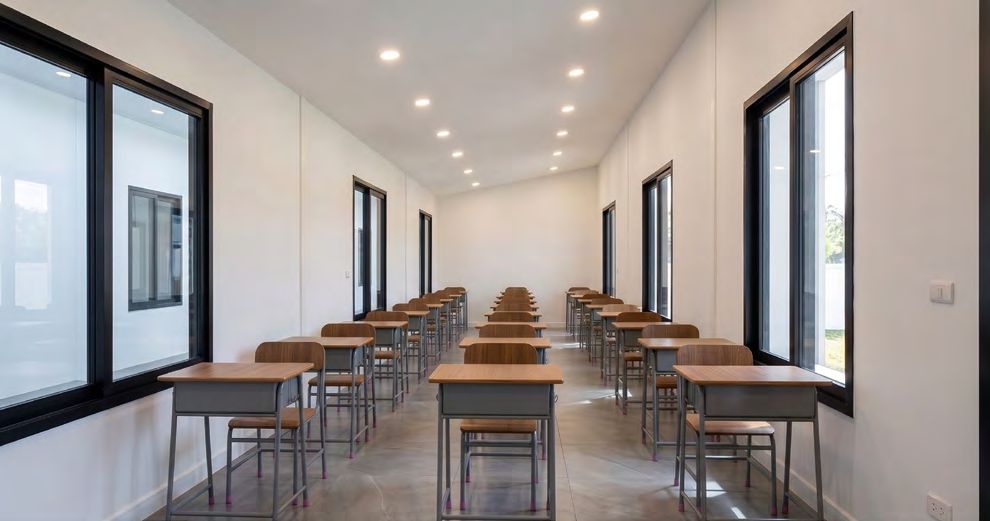 Interior of a single classroom module with rows of wooden desks and large windows